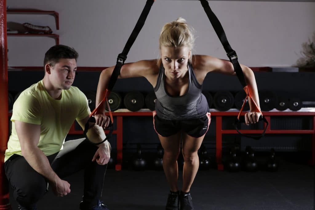 Femme qui s'entraîne avec des sangles accompagné d'un coach sportif