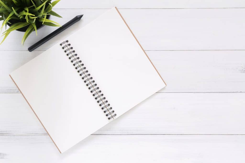 Bloc-notes posé sur une table avec un stylo noir et une plante verte